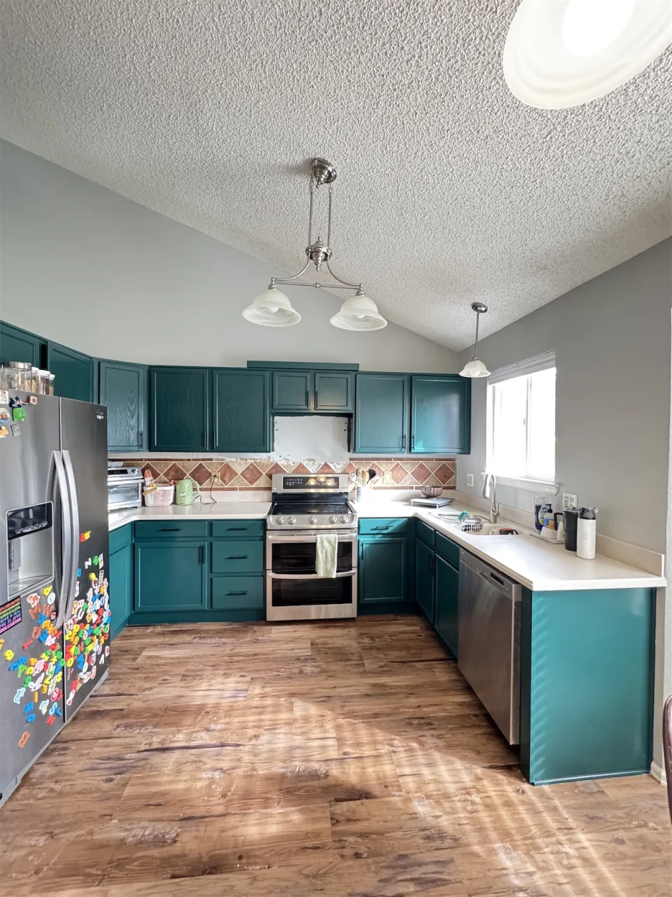 Cocina en U con gabinetes pintados en verde azulado, electrodomésticos de acero inoxidable y piso de madera clara