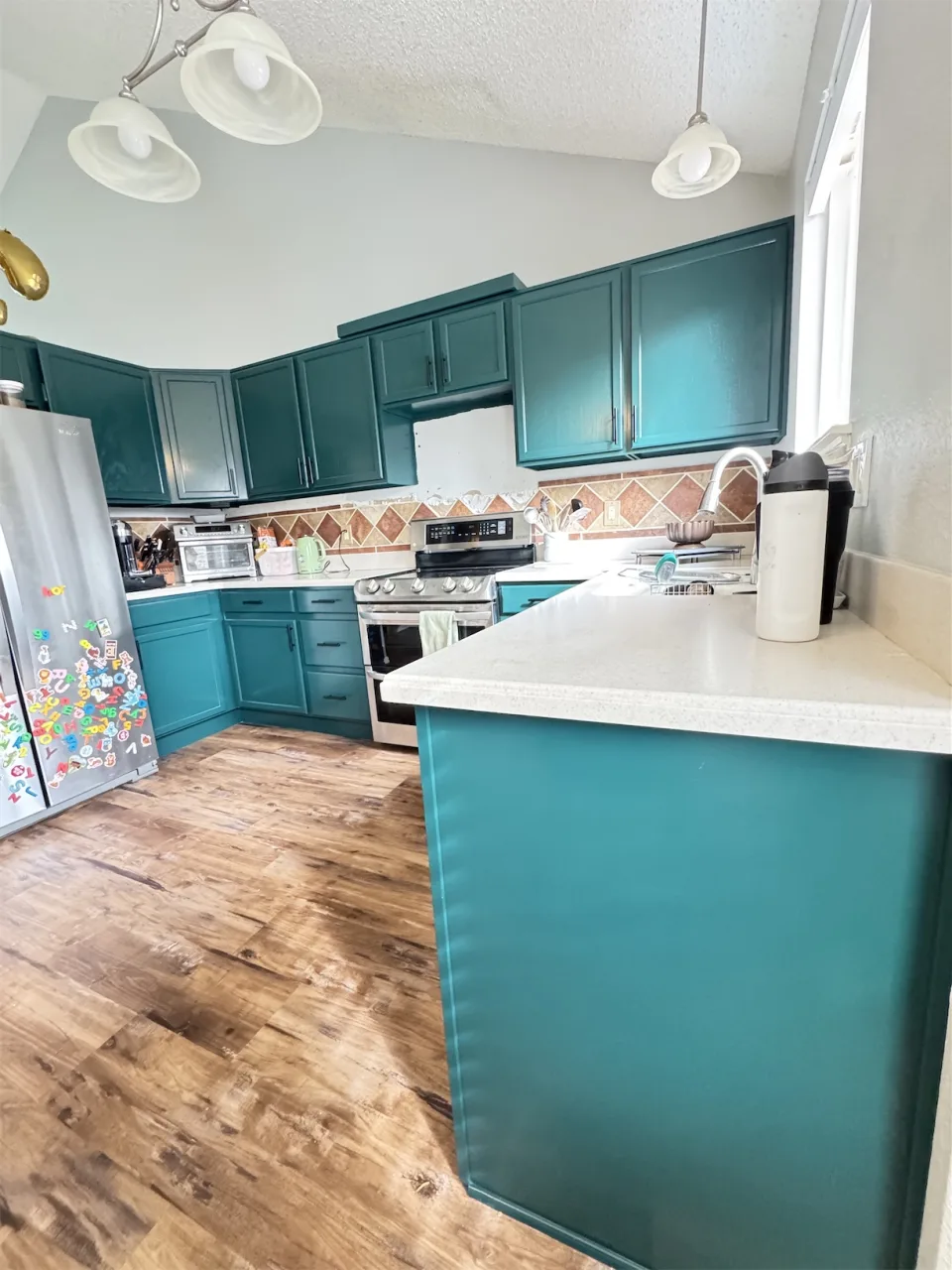 Cocina con gabinetes de madera pintados en verde azulado y península con encimera clara